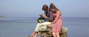 Movie still from “Pierrot le Fou” (1965), directed by Jean-Luc Godard – A man and a woman sitting next to each other on a rock; Medium shot, High angle