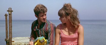 Movie still from “Pierrot le Fou” (1965), directed by Jean-Luc Godard – A man and a woman sitting next to each other on the beach; Medium shot, High angle