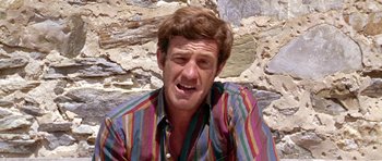 Movie still from “Pierrot le Fou” (1965), directed by Jean-Luc Godard – A person wearing a striped shirt near a stone wall; Close Up shot, High angle