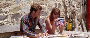Movie still from “Pierrot le Fou” (1965), directed by Jean-Luc Godard – A man and a woman sitting next to each other at a table; Medium shot, High angle