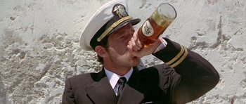 Movie still from “Pierrot le Fou” (1965), directed by Jean-Luc Godard – A man in a suit and hat drinking a beer; Close Up shot, Low angle