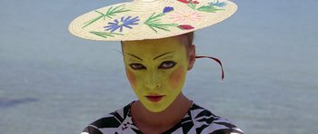 Movie still from “Pierrot le Fou” (1965), directed by Jean-Luc Godard – A woman with a painted face wearing a straw hat; Close Up shot, Overhead angle