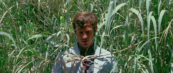 Movie still from “Pierrot le Fou” (1965), directed by Jean-Luc Godard – A man standing in tall grass looking at the camera; Medium shot, High angle