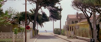 Movie still from “Pierrot le Fou” (1965), directed by Jean-Luc Godard – A person walking down a street with a surfboard; Extreme Wide shot, High angle