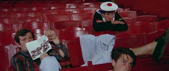 Movie still from “Pierrot le Fou” (1965), directed by Jean-Luc Godard – A man wearing a sailor's uniform sitting in a stadium seat; Medium shot, High angle