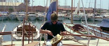 Movie still from “Pierrot le Fou” (1965), directed by Jean-Luc Godard – A man sitting on the deck of a sailboat in a marina; Wide shot, High angle