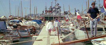 Movie still from “Pierrot le Fou” (1965), directed by Jean-Luc Godard – Two people walking on a dock near a harbor; Extreme Wide shot, High angle