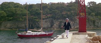 Movie still from “Pierrot le Fou” (1965), directed by Jean-Luc Godard – A woman walking a dog on a leash near a boat; Wide shot, High angle
