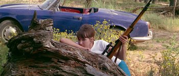 Movie still from “Pierrot le Fou” (1965), directed by Jean-Luc Godard – A young woman leaning on a fallen tree with a rifle; Medium shot, High angle