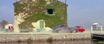 Movie still from “Pierrot le Fou” (1965), directed by Jean-Luc Godard – An old car is driving past a building with green shutters on it; Extreme Wide shot, Low angle