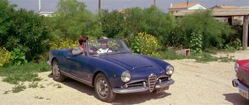 Movie still from “Pierrot le Fou” (1965), directed by Jean-Luc Godard – A man driving a blue car on a dirt road; Wide shot, High angle