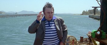 Movie still from “Pierrot le Fou” (1965), directed by Jean-Luc Godard – A man in a striped shirt and jacket holding a painting; Medium shot, Low angle