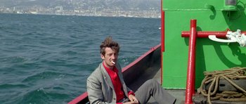 Movie still from “Pierrot le Fou” (1965), directed by Jean-Luc Godard – A man sitting on the back of a boat in the water; Medium shot, High angle