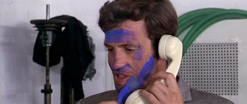 Movie still from “Pierrot le Fou” (1965), directed by Jean-Luc Godard – A man with blue paint on his face talking on a white phone; Close Up shot, Over the shoulder angle