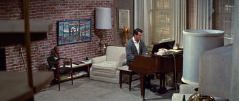 Movie still from “Pillow Talk” (1959), directed by Michael Gordon – A man sitting in front of a grand piano in a living room; Wide shot, High angle