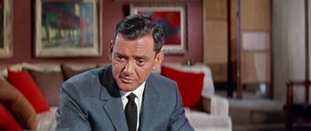 Movie still from “Pillow Talk” (1959), directed by Michael Gordon – A man in a suit and tie sitting in front of a painting; Close Up shot, Low angle