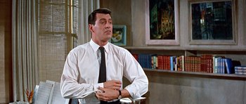 Movie still from “Pillow Talk” (1959), directed by Michael Gordon – A man sitting at a table with his hands on his chest; Medium shot, Low angle