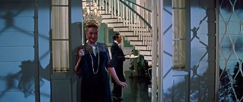 Movie still from “Pillow Talk” (1959), directed by Michael Gordon – An older woman in a dress is standing in front of a staircase; Medium shot, High angle
