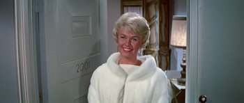 Movie still from “Pillow Talk” (1959), directed by Michael Gordon – A woman in a white coat smiling for the camera; Close Up shot, Low angle