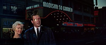 Movie still from “Pillow Talk” (1959), directed by Michael Gordon – A man in a suit and tie standing in front of a building; Medium shot, Low angle