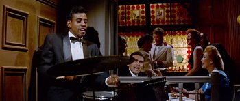 Movie still from “Pillow Talk” (1959), directed by Michael Gordon – A group of men in suits playing drums in front of a window; Medium shot, Over the shoulder angle