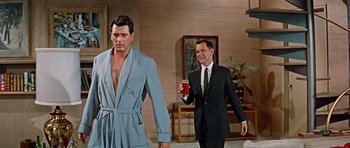Movie still from “Pillow Talk” (1959), directed by Michael Gordon – A man in a robe is holding a drink while another man in a suit stands next to him; Medium shot, Low angle
