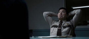 Movie still from “13 Reasons Why” (2017), created by Brian Yorkey – A man sitting at a table with his hands behind his head; Medium shot, Low angle