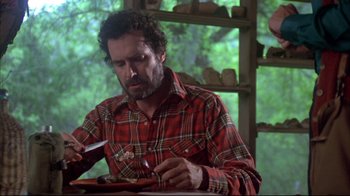 Movie still from “Piranha” (1978), directed by Joe Dante – A man sitting at a table with a plate in front of him; Medium shot, Low angle