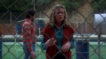 Movie still from “Piranha” (1978), directed by Joe Dante – A man and a woman standing behind a chain link fence; Medium shot, Over the shoulder angle
