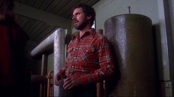Movie still from “Piranha” (1978), directed by Joe Dante – A man standing next to a wall holding a cell phone; Medium shot, Low angle