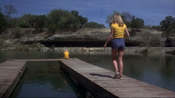 Movie still from “Piranha” (1978), directed by Joe Dante – A woman standing on a pier next to a fire hydrant; Wide shot, Over the shoulder angle