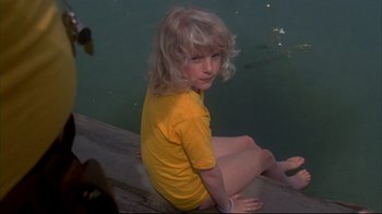 Movie still from “Piranha” (1978), directed by Joe Dante – A young girl sitting on a dock by a body of water; Medium shot, High angle