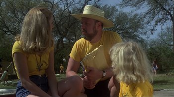 Movie still from “Piranha” (1978), directed by Joe Dante – A man sitting on the ground with two children; Medium shot, Over the shoulder angle