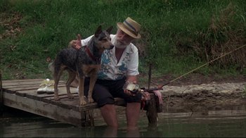 Movie still from “Piranha” (1978), directed by Joe Dante – An older man sitting on a dock with a dog; Wide shot, Low angle