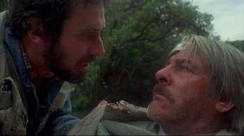 Movie still from “Piranha” (1978), directed by Joe Dante – Two men are looking at each other in a forest; Close Up shot, Low angle