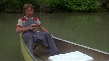 Movie still from “Piranha” (1978), directed by Joe Dante – A young boy sitting in a boat on a river; Medium shot, High angle