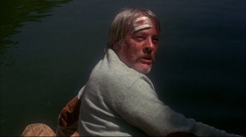 Movie still from “Piranha” (1978), directed by Joe Dante – A man with a bandage on his head is sitting in the water; Close Up shot, High angle