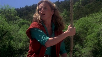 Movie still from “Piranha” (1978), directed by Joe Dante – A woman holding a stick in a wooded area; Medium shot, Low angle
