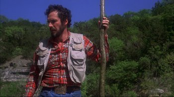 Movie still from “Piranha” (1978), directed by Joe Dante – A man holding a stick in a forest; Medium shot, Low angle