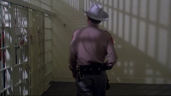 Movie still from “Piranha” (1978), directed by Joe Dante – A man in a uniform and a white hat is standing in a jail cell; Wide shot, Low angle