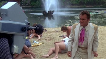Movie still from “Piranha” (1978), directed by Joe Dante – A group of people sitting on the sand near a body of water; Wide shot, Low angle