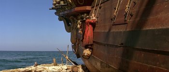 Movie still from “Pirates” (1986), directed by Roman Polanski – A man hanging on to the side of an old boat; Wide shot, Low angle