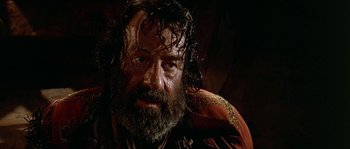 Movie still from “Pirates” (1986), directed by Roman Polanski – A man with a beard and a red jacket is looking at the camera; Close Up shot, High angle