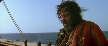 Movie still from “Pirates” (1986), directed by Roman Polanski – A man with long hair and a beard standing on a beach near the ocean; Medium shot, Over the shoulder angle
