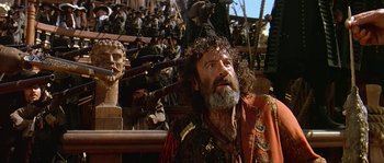 Movie still from “Pirates” (1986), directed by Roman Polanski – An old man with a beard and a long beard is sitting in front of a group of people; Medium shot, Low angle