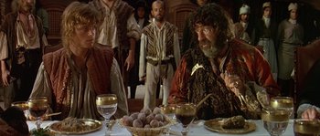 Movie still from “Pirates” (1986), directed by Roman Polanski – A group of people standing around a table; Medium shot, Over the shoulder angle