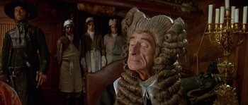 Movie still from “Pirates” (1986), directed by Roman Polanski – An old man in a wig and wig stand in front of a group of men; Medium shot, Over the shoulder angle