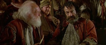 Movie still from “Pirates” (1986), directed by Roman Polanski – A group of men sitting next to each other in a room; Medium shot, Over the shoulder angle