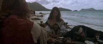 Movie still from “Pirates” (1986), directed by Roman Polanski – A woman dressed as a pirate sitting at a table on the beach; Medium shot, High angle