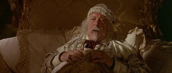 Movie still from “Pirates” (1986), directed by Roman Polanski – An old man with a white beard wearing a hat and sitting on a couch; Medium shot, High angle